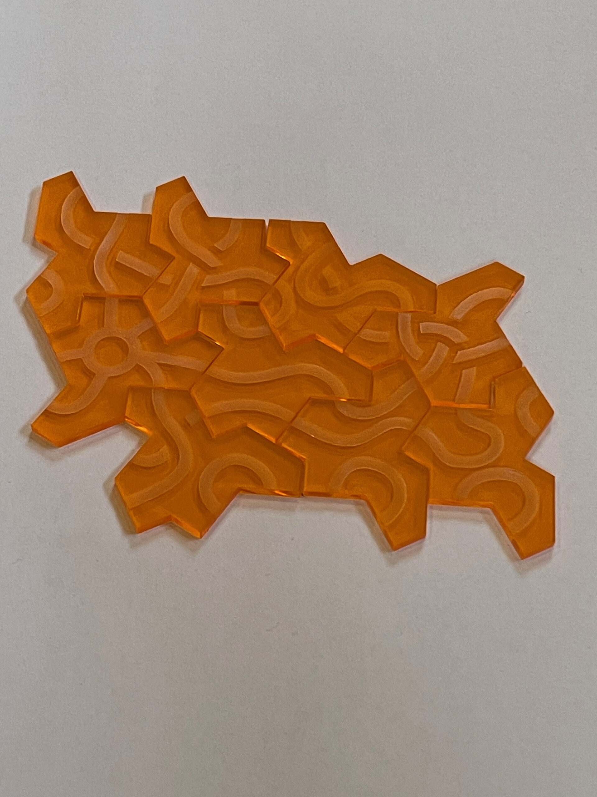 Einstein tiles cut from transparent orange acrylic showing engraved road network